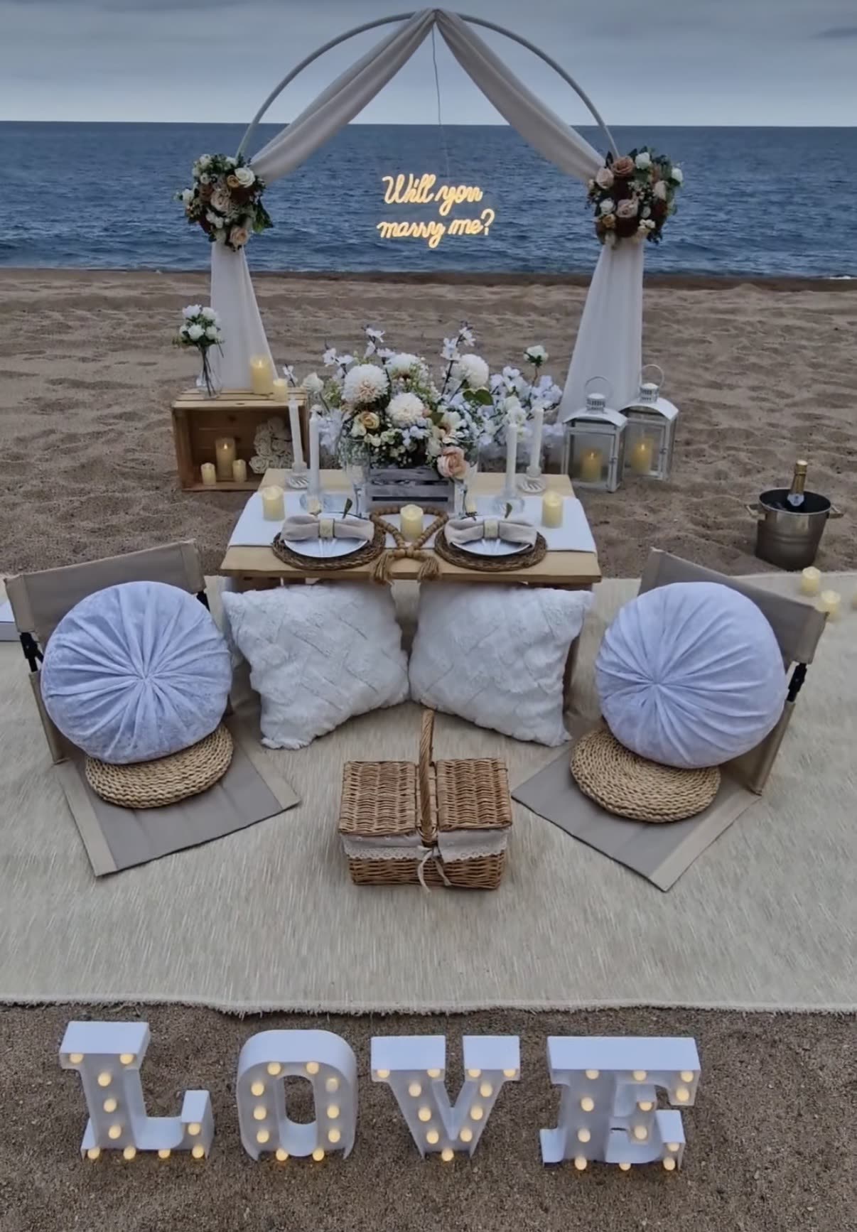 Beach proposal setup with floral arch and LOVE letters